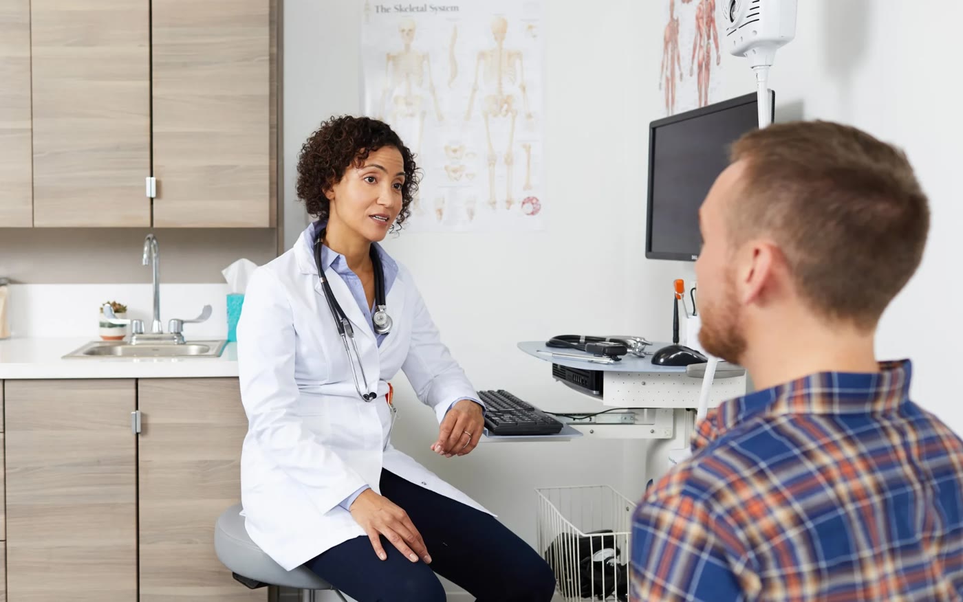 Final photo: a doctor in a white coat talking with a patient in a plaid shirt in a bright exam room
